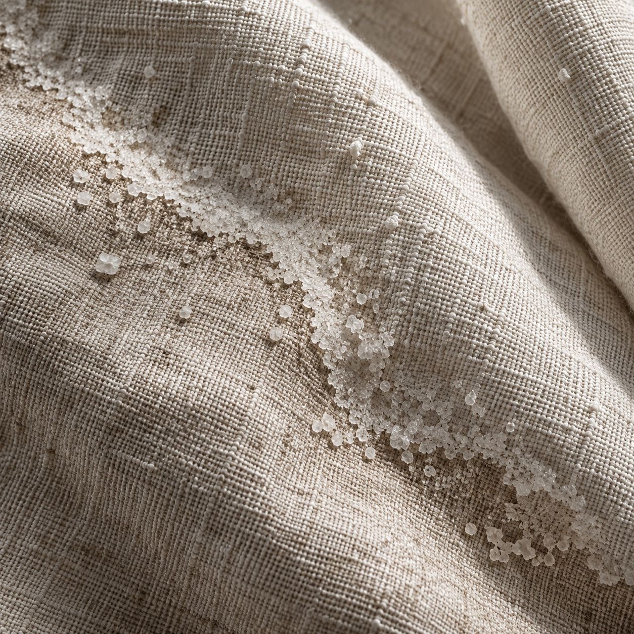 Extreme close-up of bone salt-washed linen with a pale crystalline tide mark running across the weave